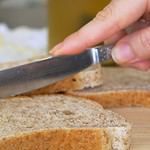 Close Up shot of a knife spreading butter on a piece of bread, tasty food being prepared for breakfast or lunch. Spreading Vegan Butter On Rye Bread Without Dairy And Eggs.