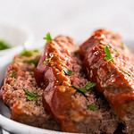 Slicing classic meatloaf with a sweet glaze on a white serving plate