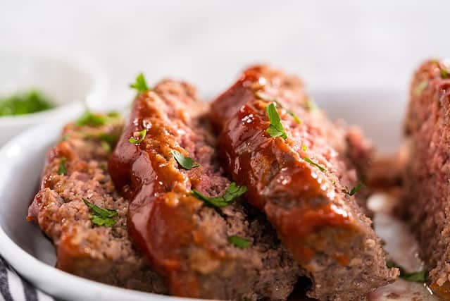 Slicing classic meatloaf with a sweet glaze on a white serving plate