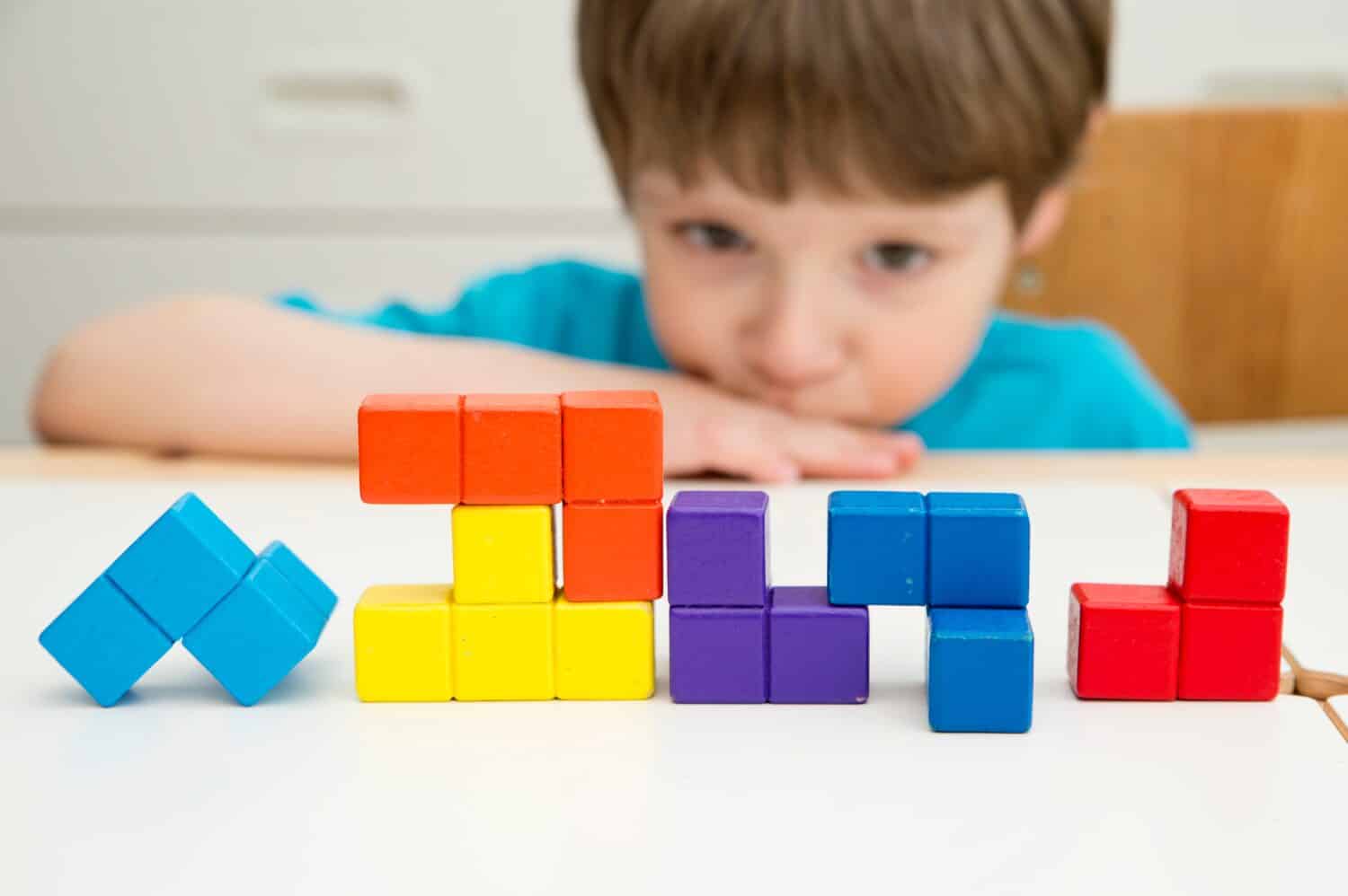 Wooden colorful blocks similar to popular  ‎tile-matching puzzle game. Boy matching figures to create new shapes. Montessori type logical game for kids. Brain exercise for preschoolers.   