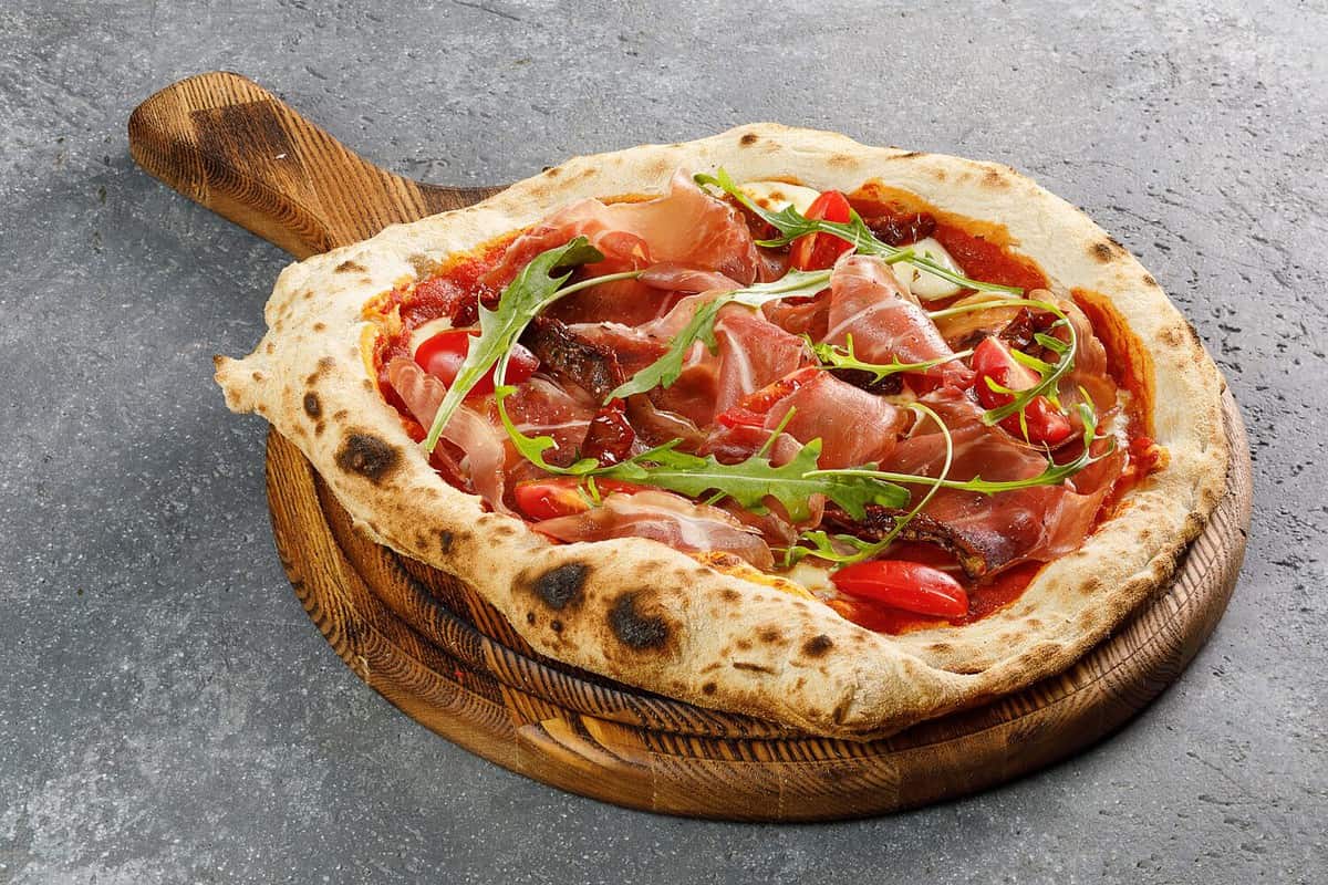 Overhead view of Napoli pizza with proscuitto on wooden board