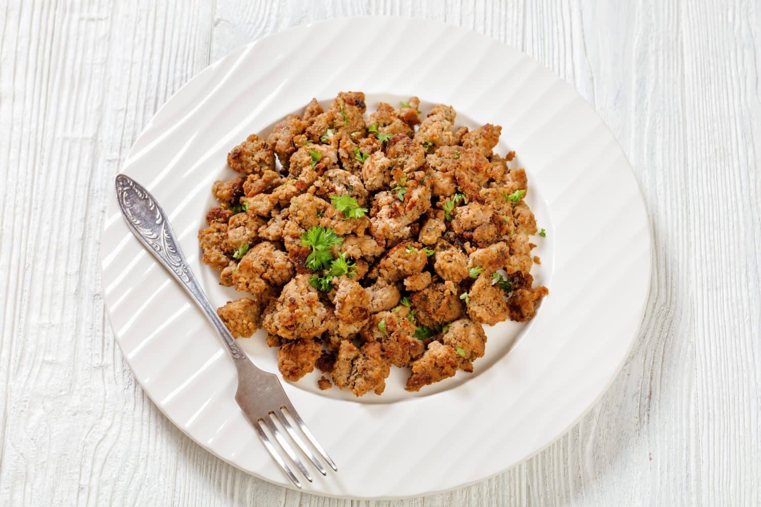 fried Italian sausage of freshly ground pork meat and spices on white plate with fork on white wooden textured table, horizontal view from above