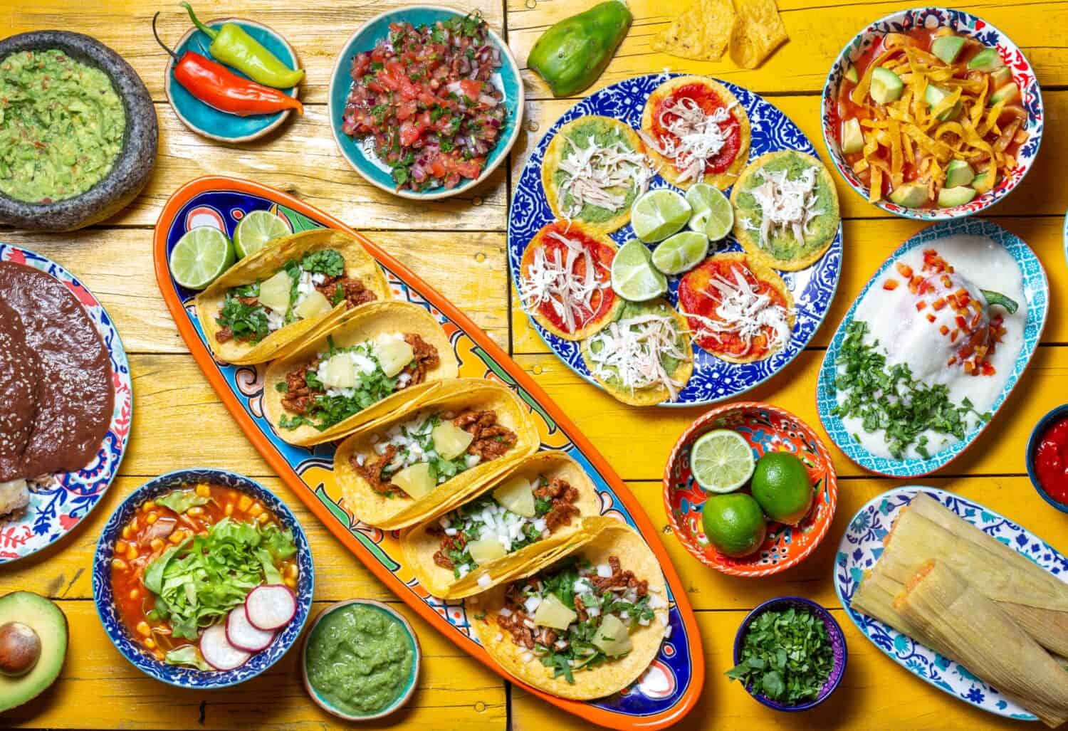 Mexican festive food for independence day - independencia chiles en nogada, tacos al pastor, chalupas pozole, tamales, chicken with mole poblano sauce. Yellow background