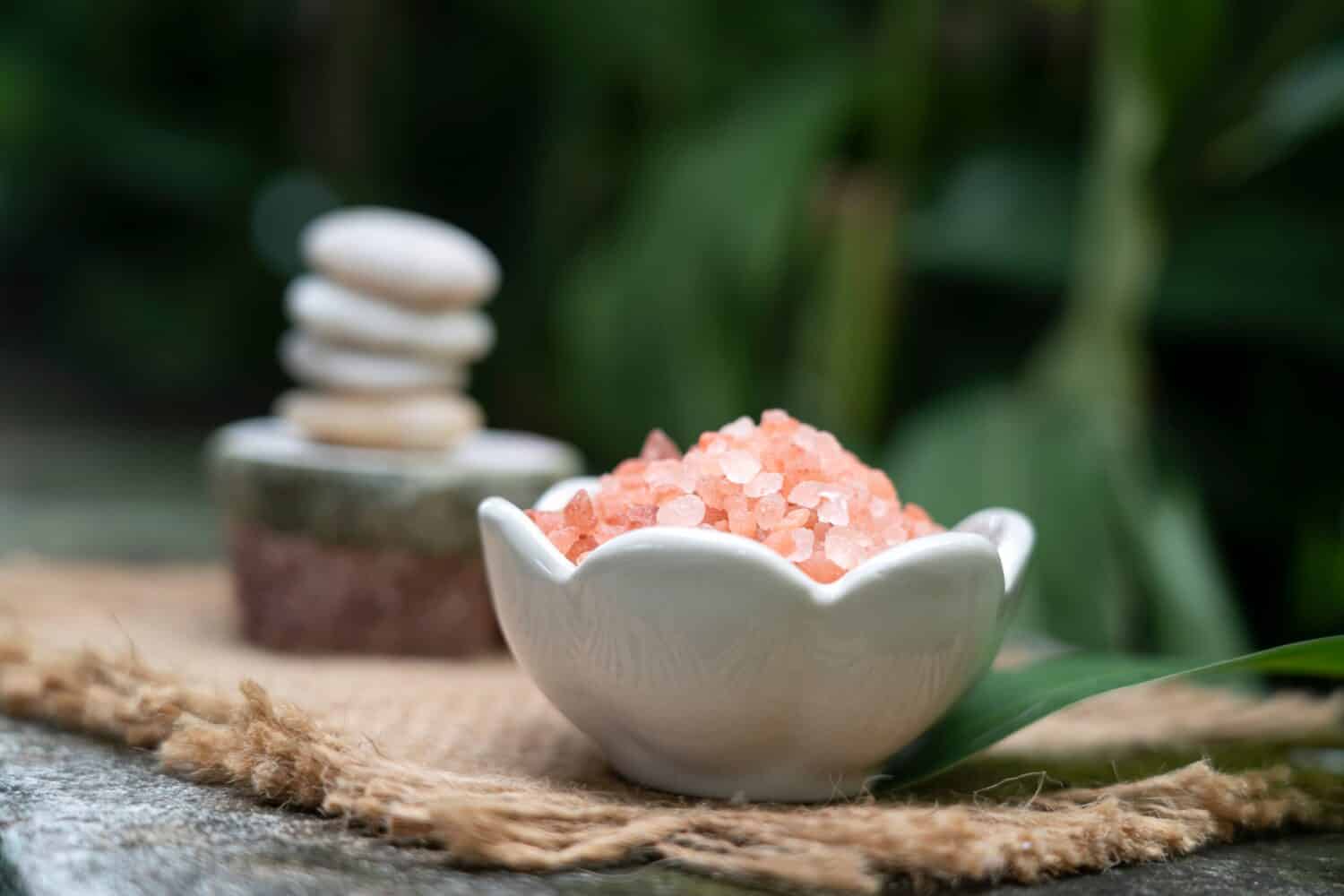 pink himalayan salt in white ceramic bowl in front of  meditation stack stone  on green blurred background,  aromatherapy spa set concept. 