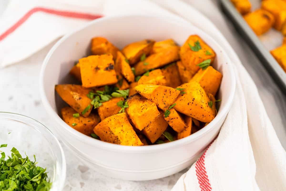 Serving oven-roasted sweet potatoes in a white ceramic bowl.