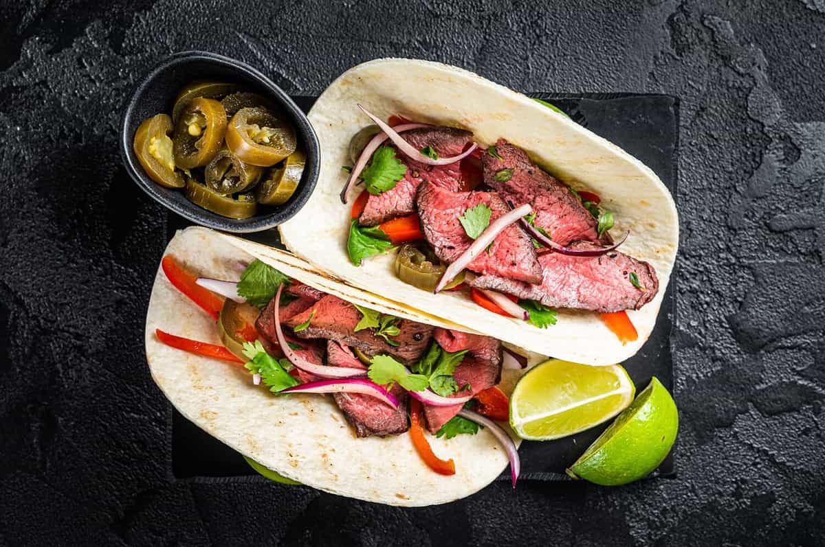 Mexican Steak Tacos with beef meat, cilantro, green sauce, jalapenos and onion. Black background. top view.