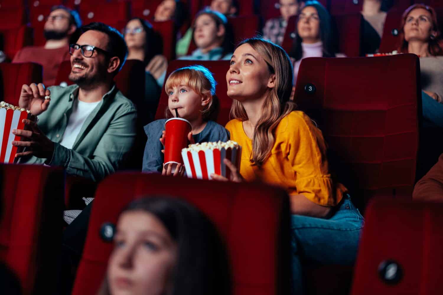 A young Caucasian family in in a movie theater watching a film together and having a good time.