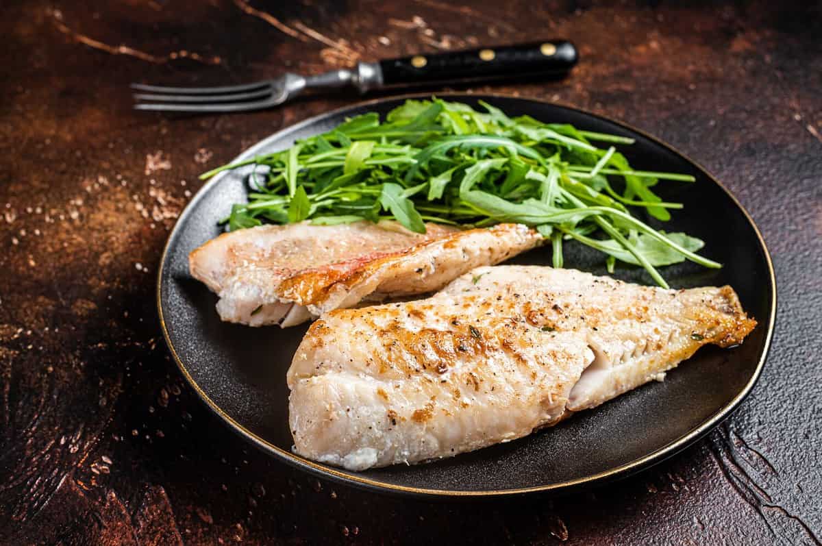 Roasted Snapper, sea red perch fillet on a plate with salad. Dark background. Top view.