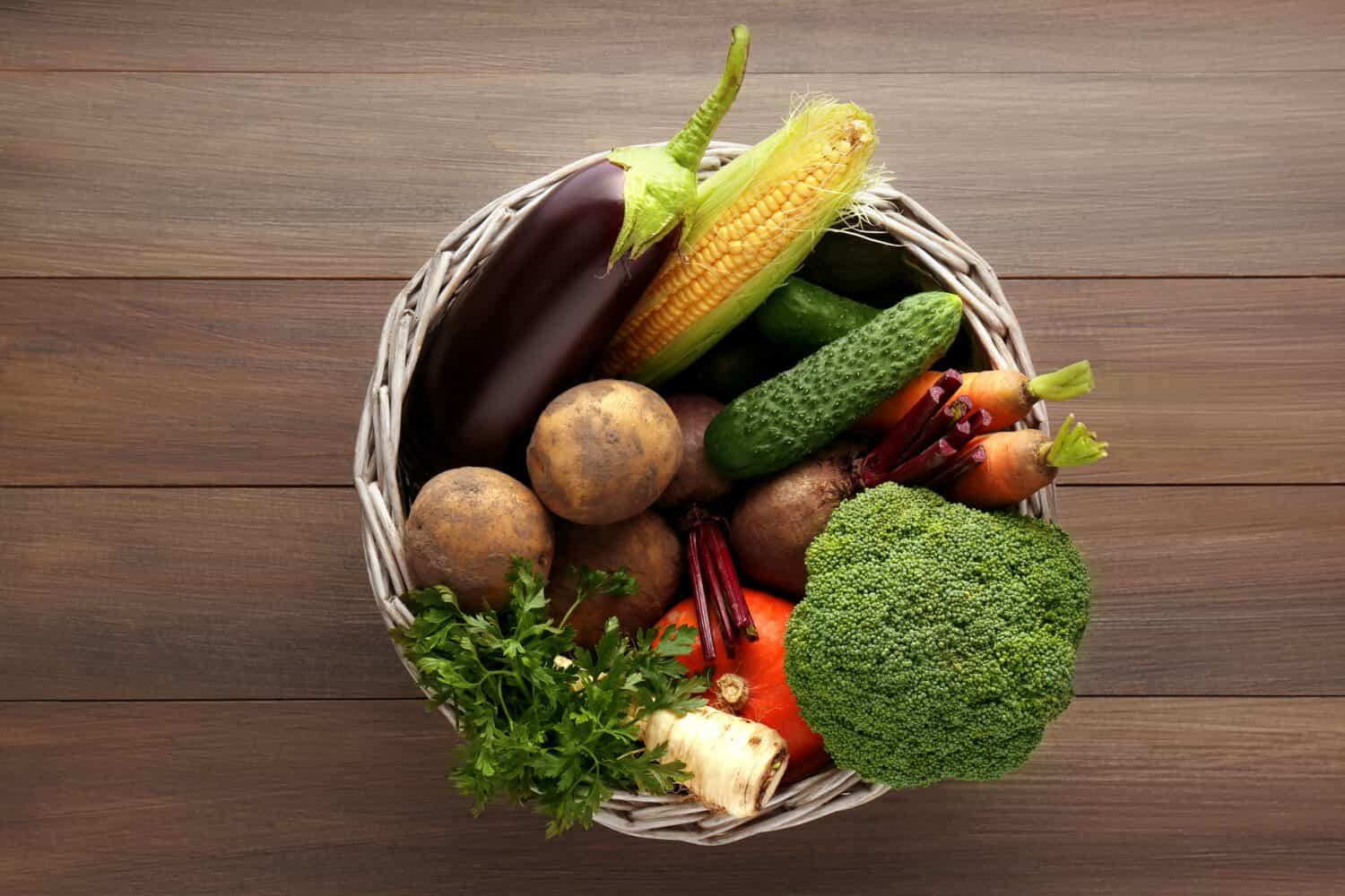 Basket with different fresh ripe vegetables on wooden table, top view. Farmer produce