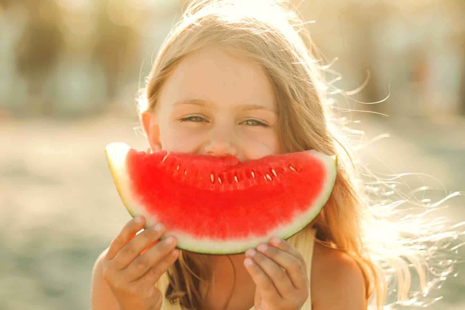 Portrait happy excited funny child little girl eat piece of juice watermelon on beach. Concept of summertime and picnic outdoors. Banner, copy space, place fot text,isolated. Nature background