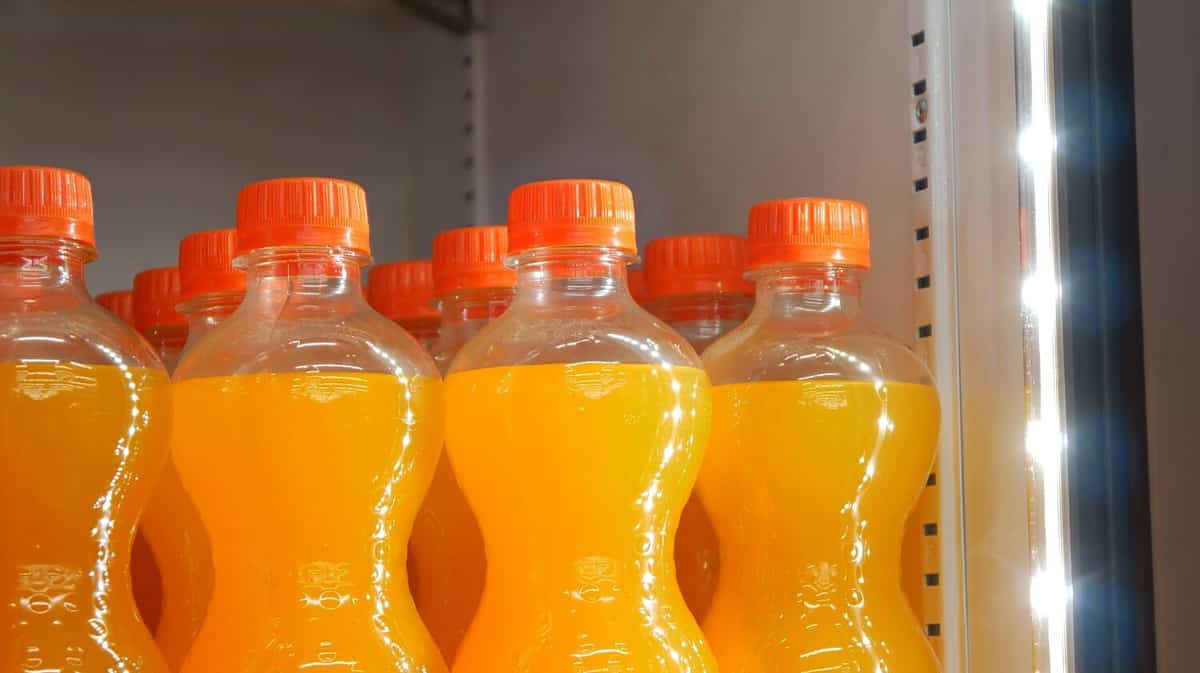 Close-up of many orange soda bottles in a store fridge