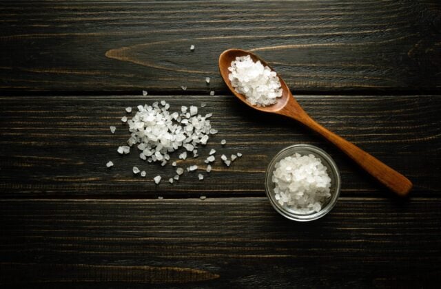 Coarse sea salt in a wooden spoon and on a vintage table. Traditional medicine concept