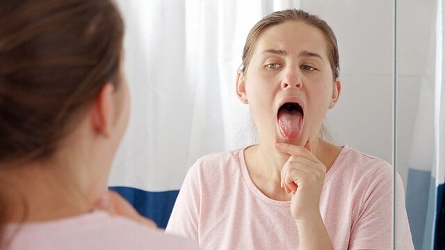 Portrait of young brunette woman checking her tongue for plaque and microbes while looking in mirror.