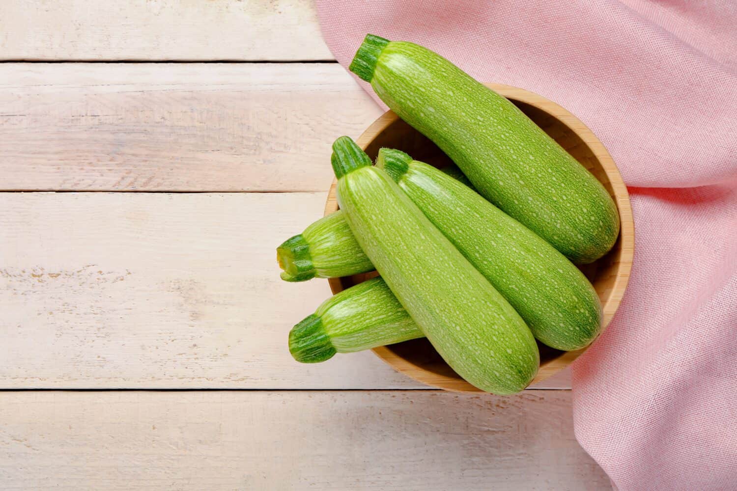 Bowl with many fresh green zucchini on white wooden background