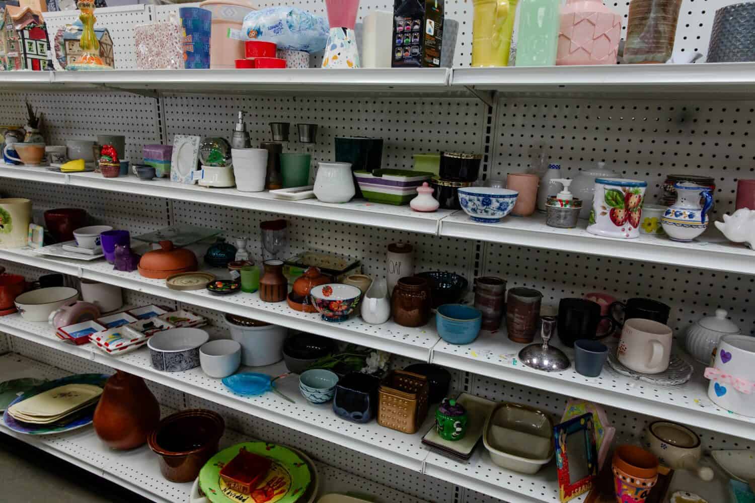 assorted donated second hand household items, arranged on shelves on display in a thrift store. Thrifting