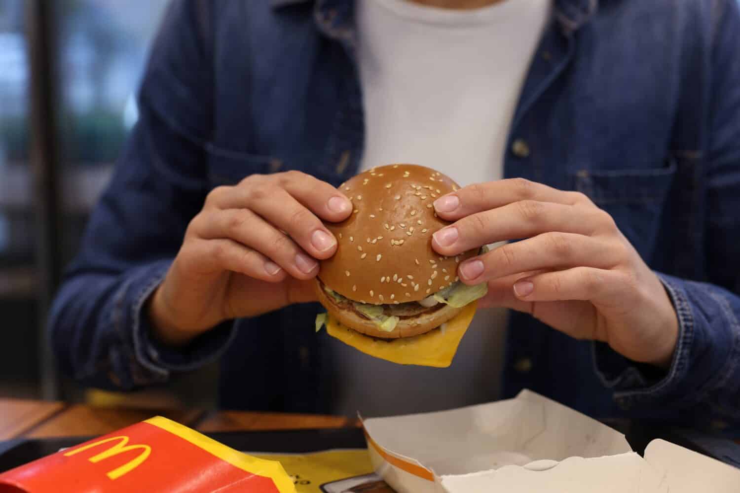 Lviv, Ukraine - October 9, 2023: Woman with McDonald's burger at table in restaurant, closeup