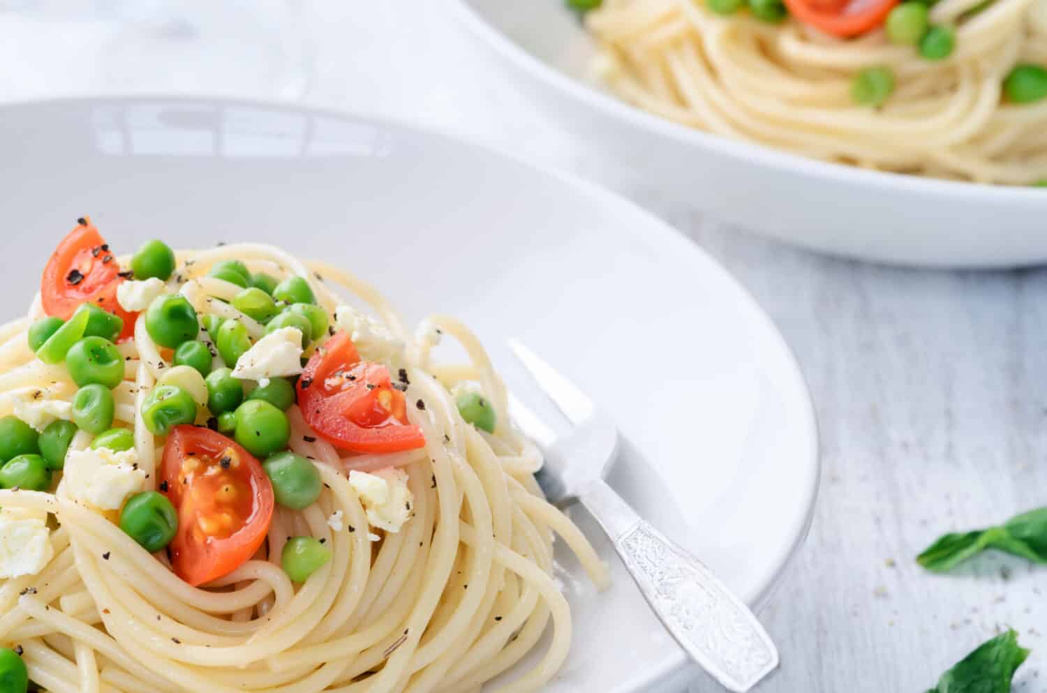 Bowls of delicious pasta topped with cherry tomatoes, peas and feta cheese 