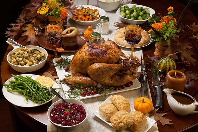 Roasted turkey garnished with cranberries on a rustic style table decoraded with pumpkins, gourds, asparagus, brussel sprouts, baked vegetables, pie, flowers, and candles.