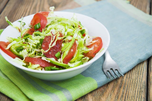 Salad with fresh cabbage, tomato, cucumber and herbs on the plate on a table