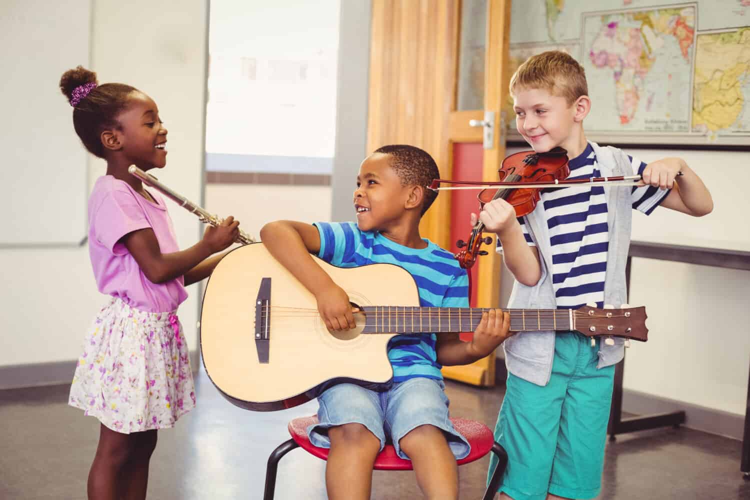 Smiling kids playing guitar, violin, flute in classroom at school