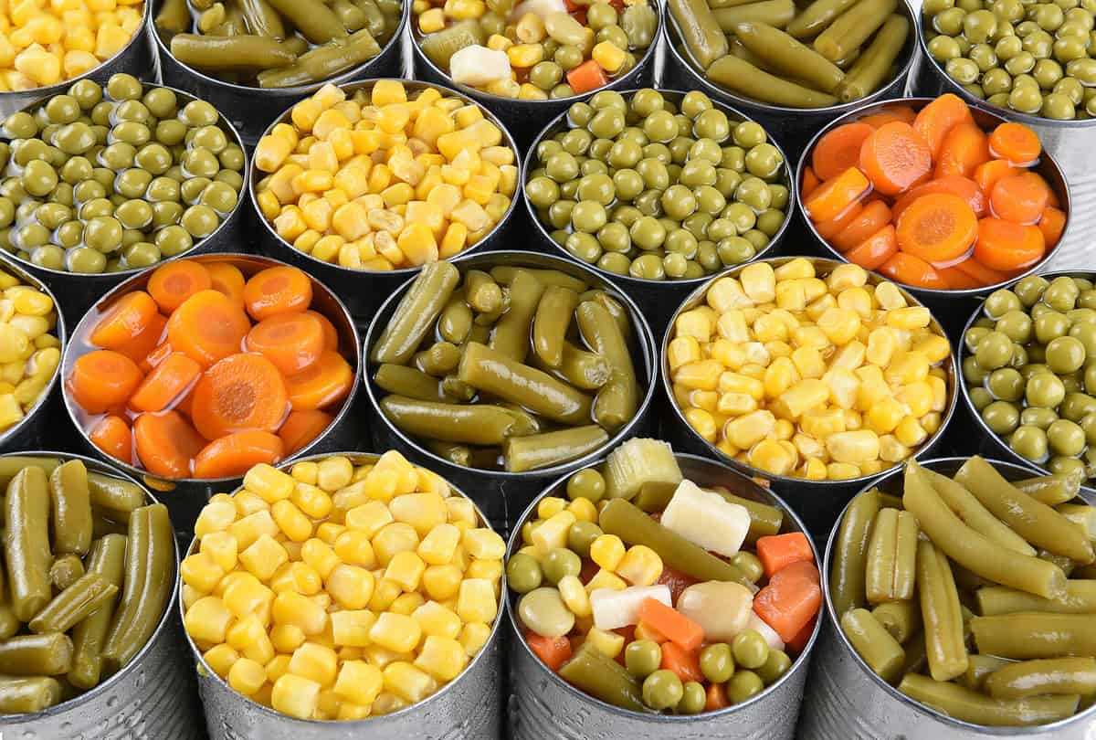 Closeup shot of cans of vegetables. Corn, Peas, Green beans, carrots in open cans filling the frame.