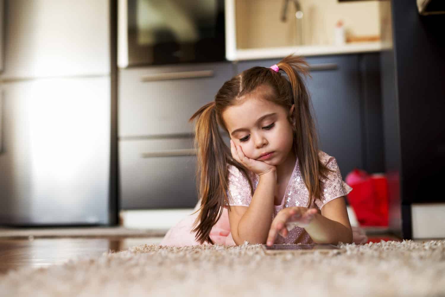 Bored little girl looking at tablet. Loneliness childhood.