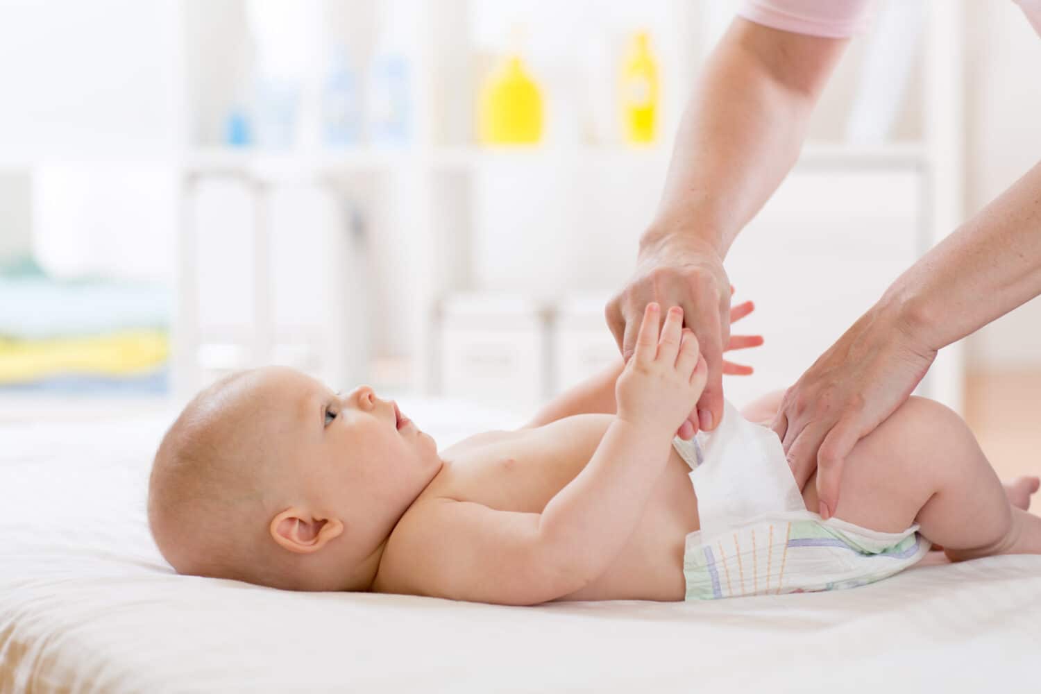 Mother putting diaper on her happy baby in nursery