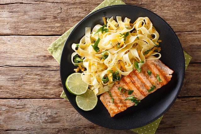 Pasta fetuccini with cheddar cheese and grilled salmon on a plate close-up. horizontal view from above