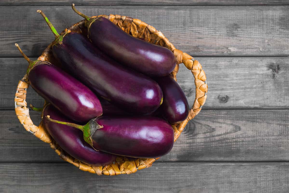 Fresh raw Purple Eggplant in a special wicker basket for Eggplant on gray wooden background. Top view, blank space.