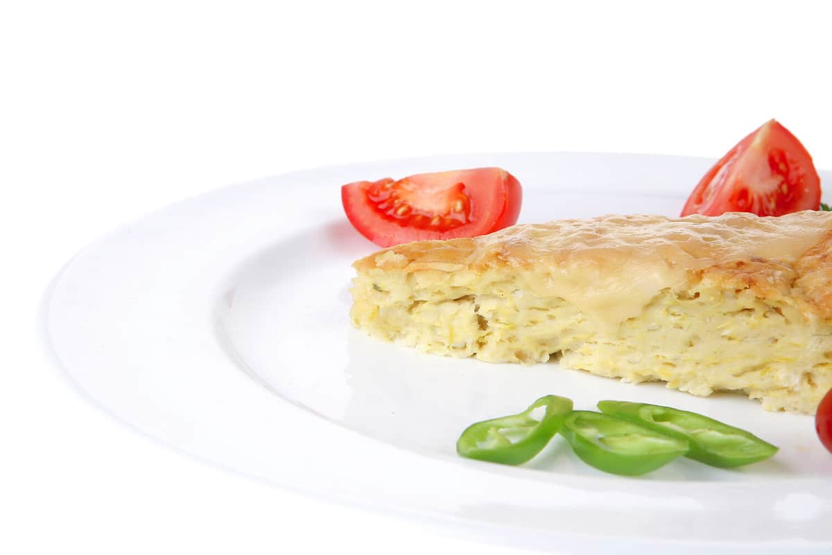 food : vegetable casserole triangle on white plate with cheese and tomatoes isolated on white background with red and green hot peppers