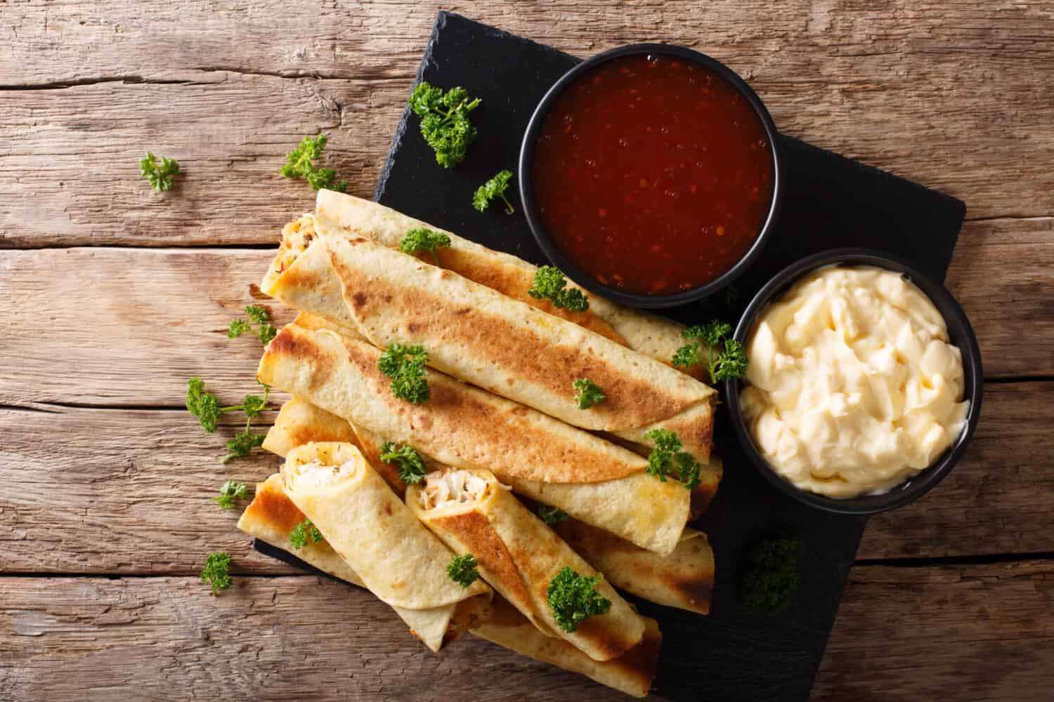 Mexican taquitos with chicken and cheese stuffing close-up, and sauces on the table. horizontal top view from above