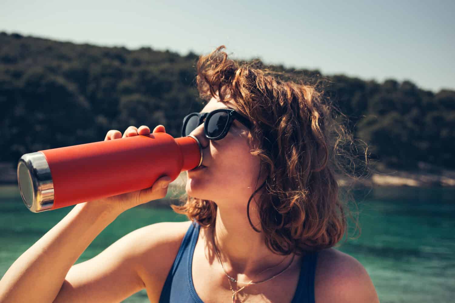 A beautiful girl drinking from a steel water bottle at the beach