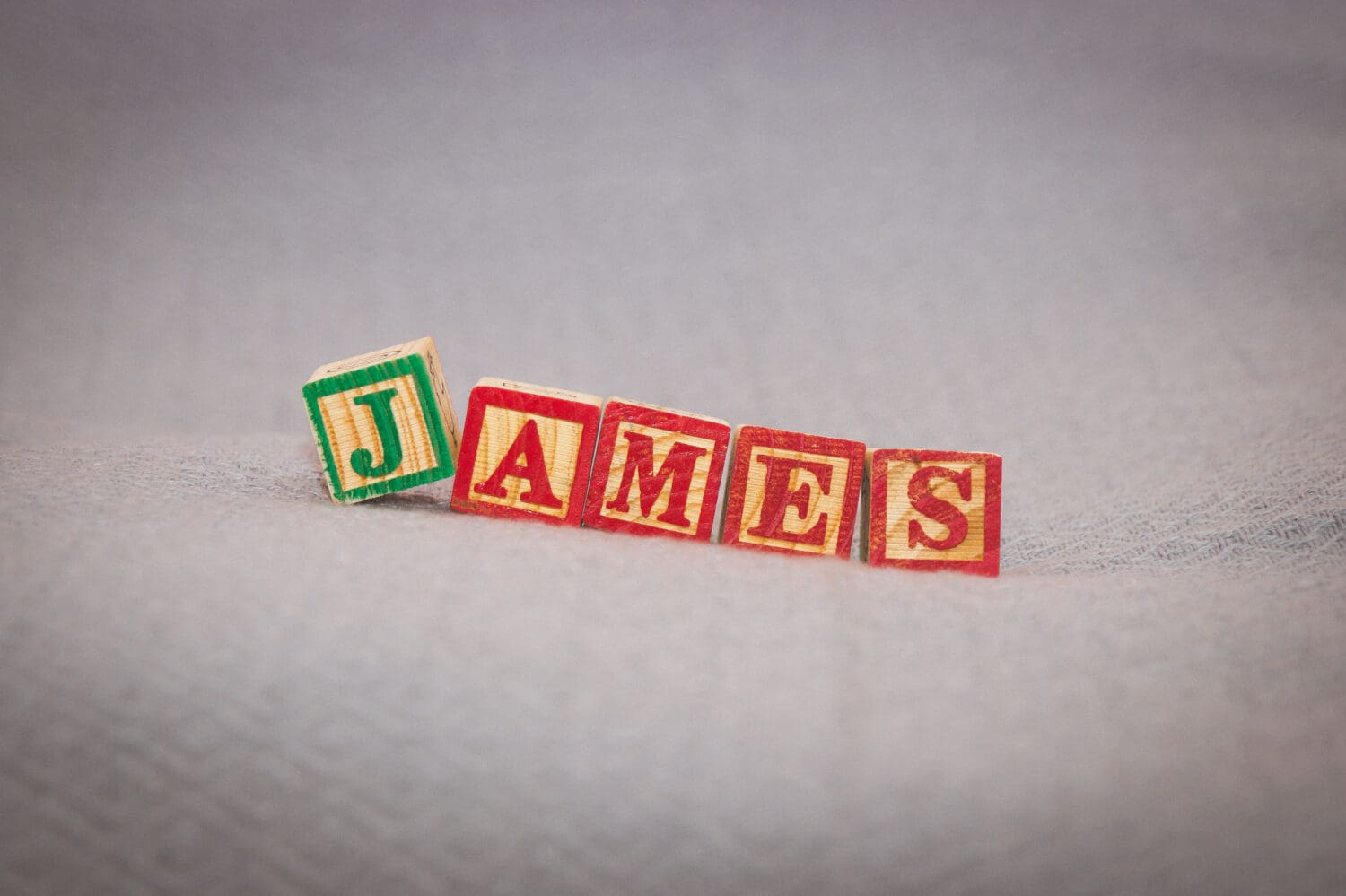 Boy's baby name James in wooden toy blocks in red and green on blanket closeup
