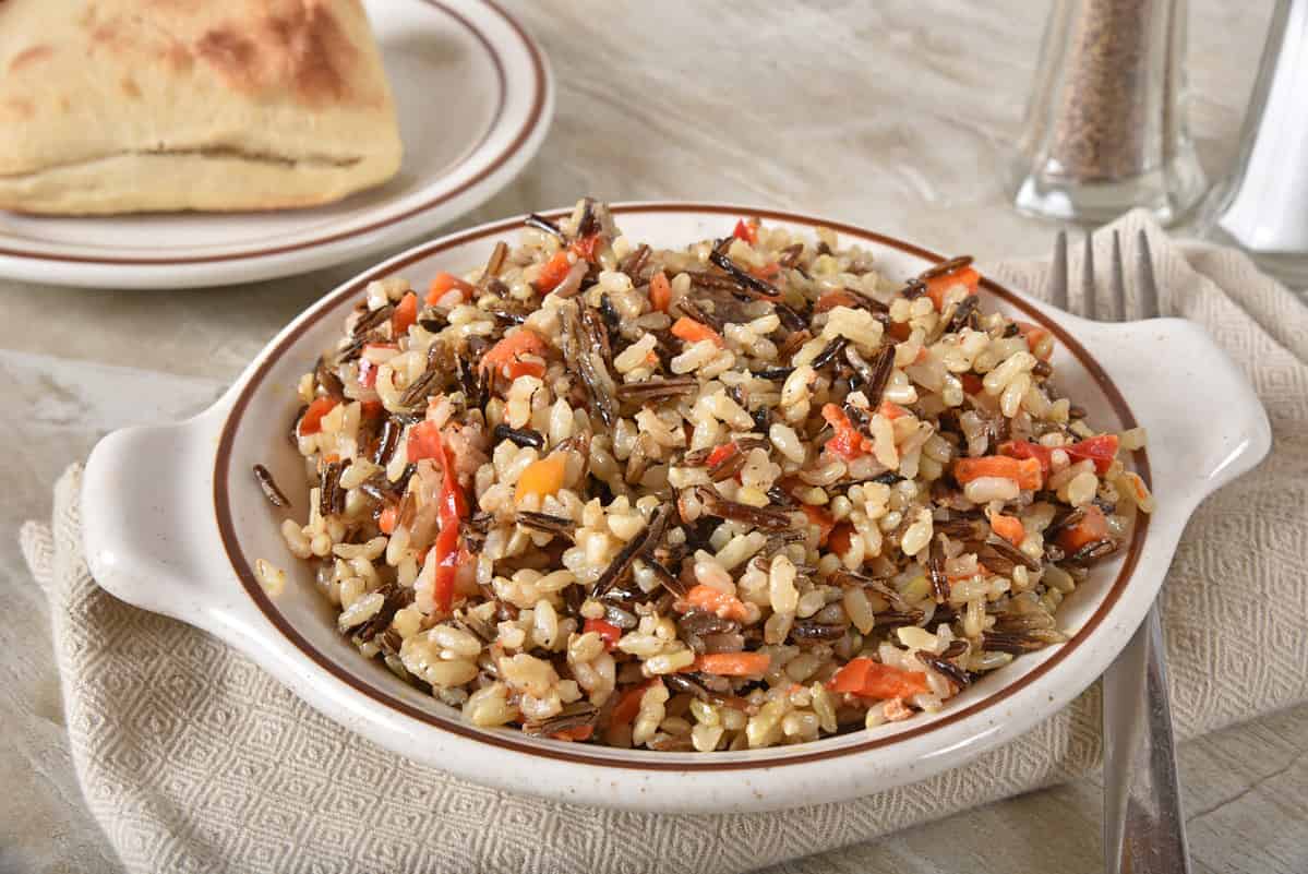 Gourmet wild rice pilaf with carrots, peppers, and sauce with a dinner roll.