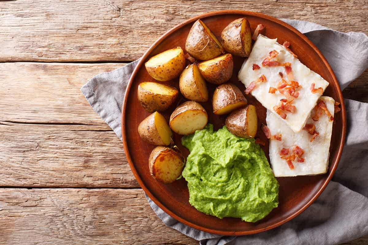 Popular Scandinavian food Lutefisk cod with pea puree, baked potatoes and bacon close-up on a plate on the table. Horizontal top view from above