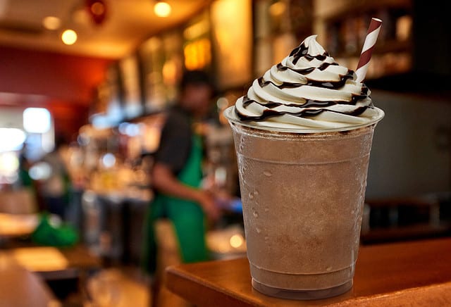 Cup of iced medium coffee or Frappuccino with cream and chocolate sauce on wooden counter at cafe or coffee shop.