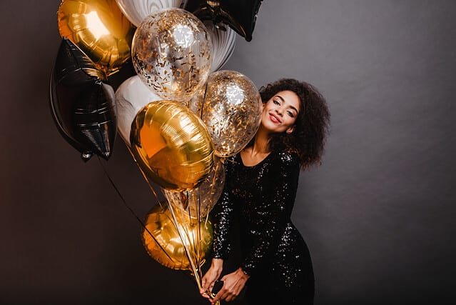 Romantic african girl holding bunch of party balloons. Indoor shot of graceful black lady celebrating birthday.