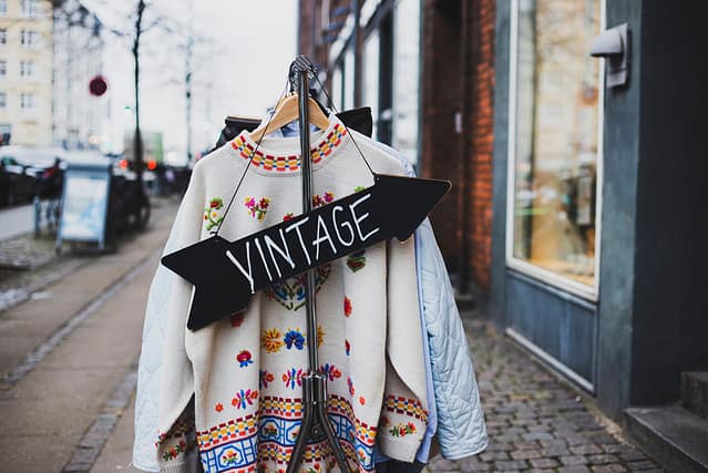 Vintage sign with a background of different vintage clothing on a street. White vintage sweater with embroidered flowers.