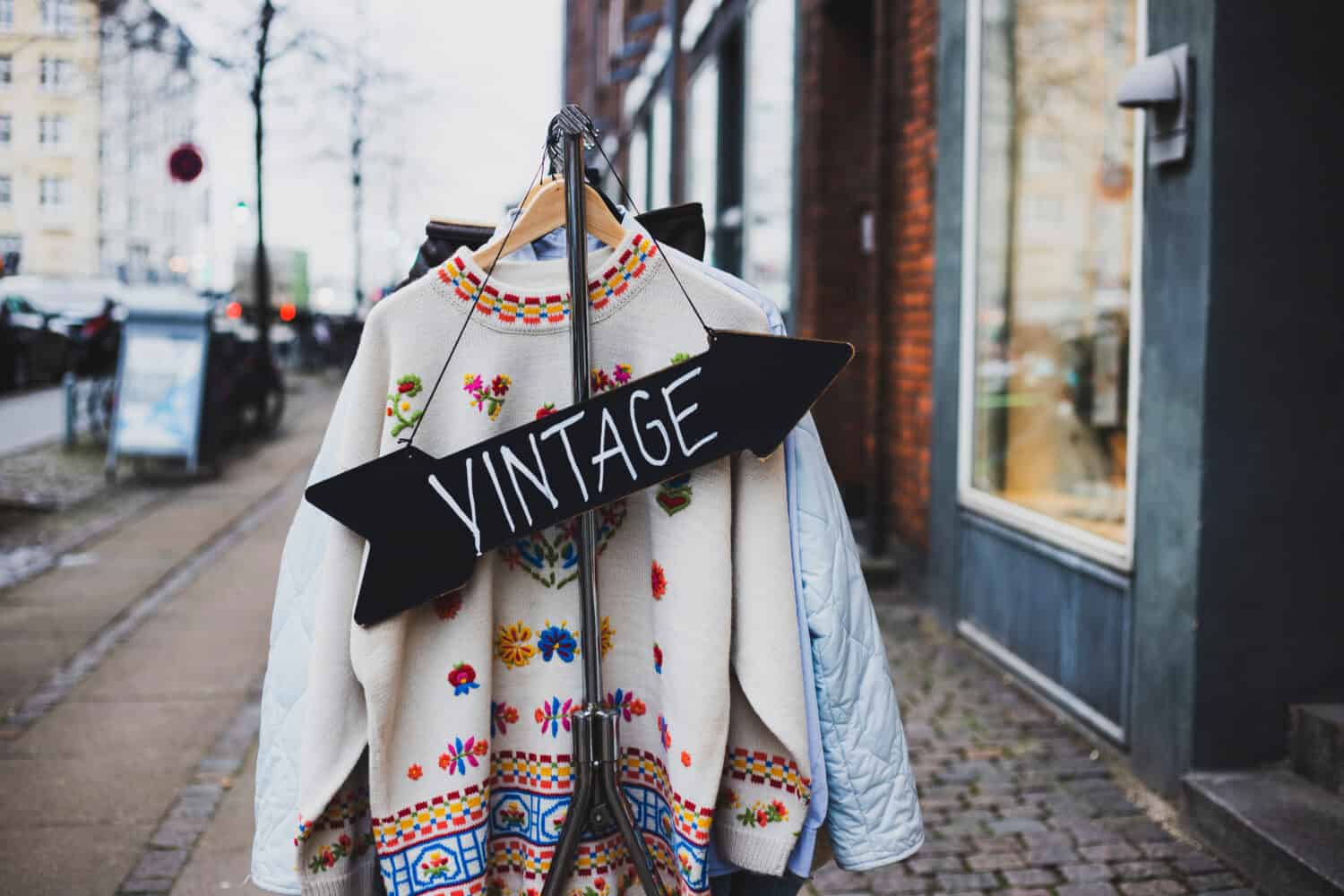 Vintage sign with a background of different vintage clothing on a street. White vintage sweater with embroidered flowers.  