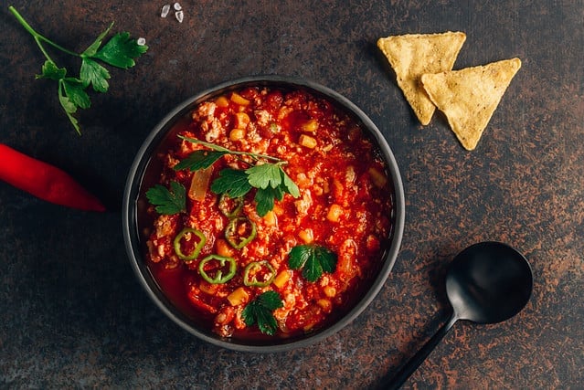 Chili Con Carne in bowl with tortilla chips on dark background. Mexican cuisine. Top view