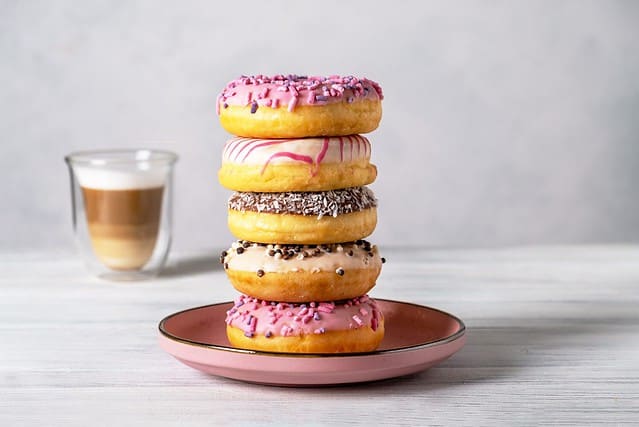 Glazed decorated donuts on plates and coffee latte or cappuccino with milk foam in a heat-resistant glass cup. Selective focus.