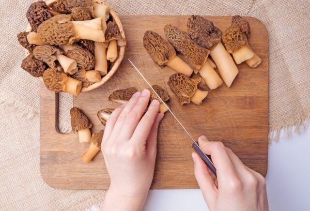 Cook slices morel mushrooms on a chopping board, top view
