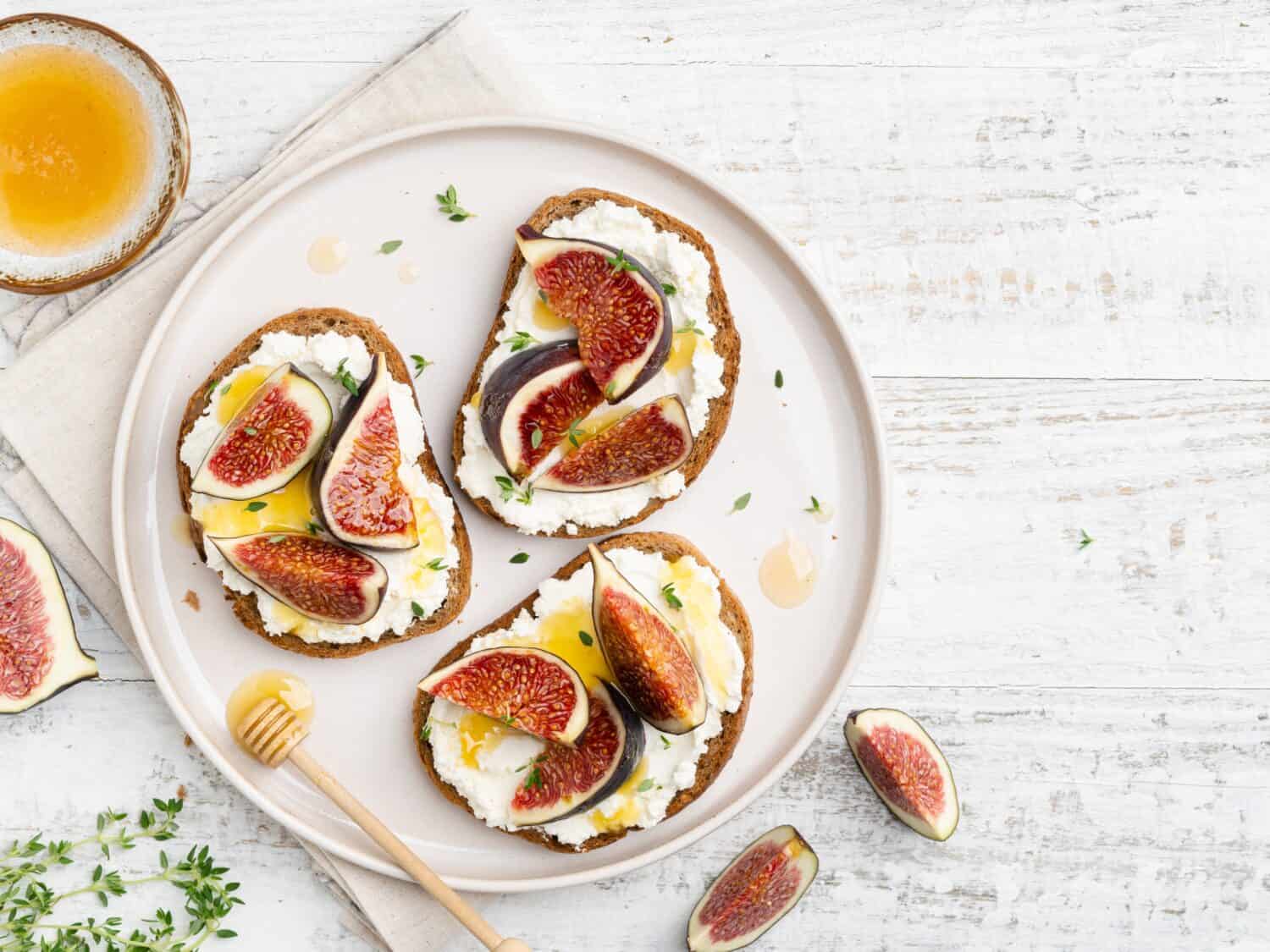 Ricotta, figs and honey bruschetta. Open sandwiches (toasts) with cream cheese, fresh sliced figs, syrup and thyme leaves. Tasty morning breakfast, lunch or dessert. Healthy eating concept. Top view.