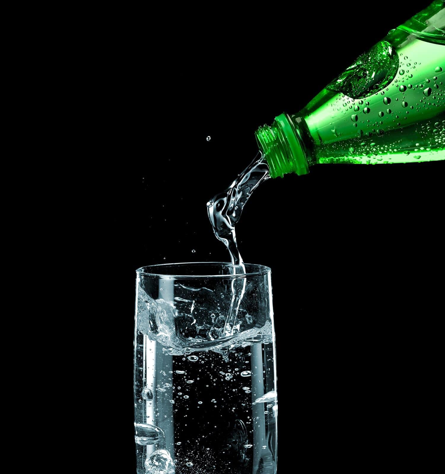 Pouring sparkling water in a glass from a green plastic bottle on black background