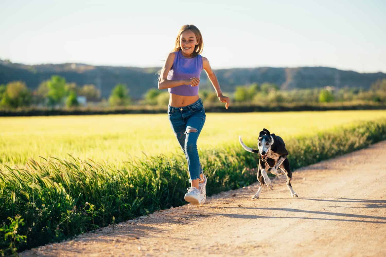 Beautiful young blonde woman running in the field with her greyhound dog.