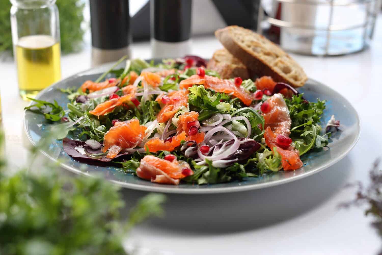 Salad with smoked salmon, onion and pomegranate seeds, on a blue plate, close-up, selective focus. Light, healthy lunch with vegetables and fish, served with bread.