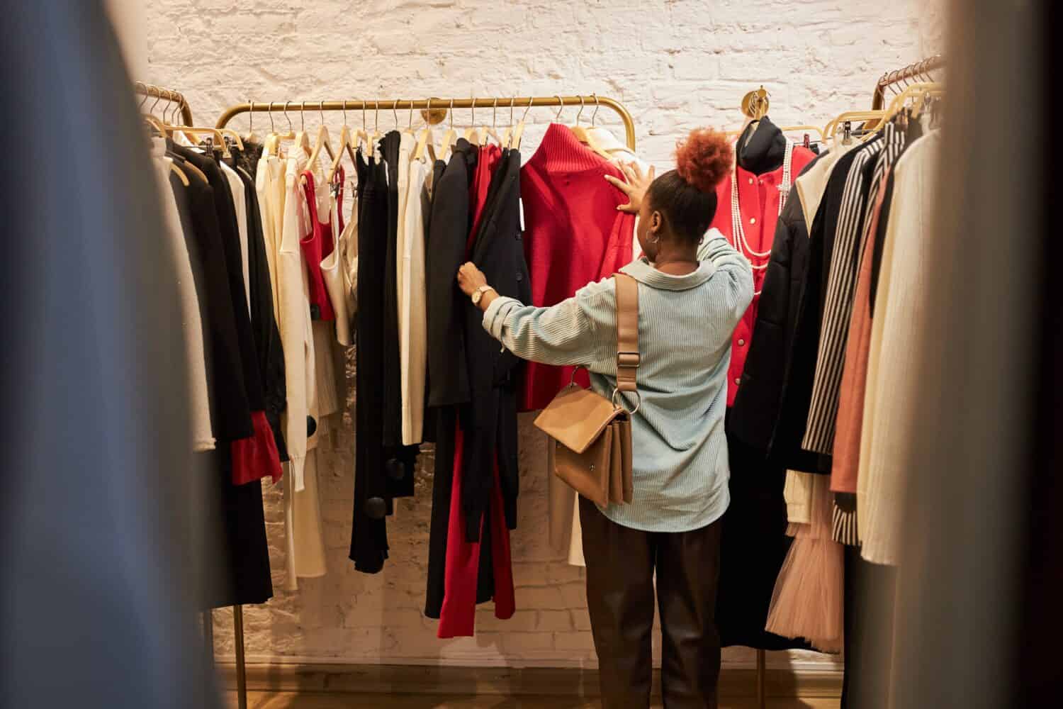 Back view at young woman browsing clothing racks in boutque or second hand shop, copy space