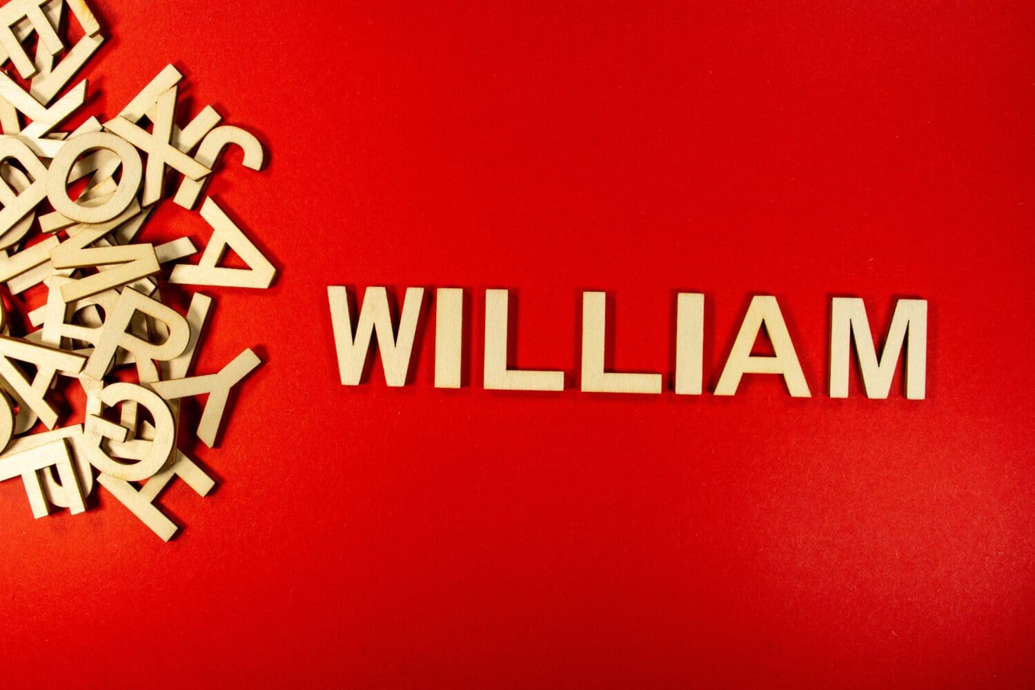 Popular and modern baby boy fashion name WILLIAM in wooden English language capital letters spilling from a pile of letters on a red background