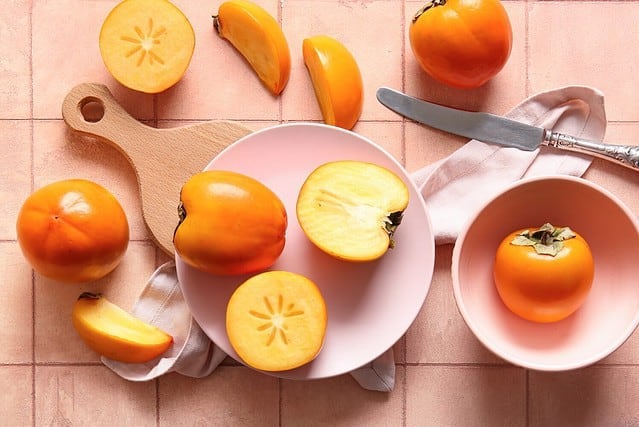 Plate and bowl with sweet ripe persimmons on pink tile background