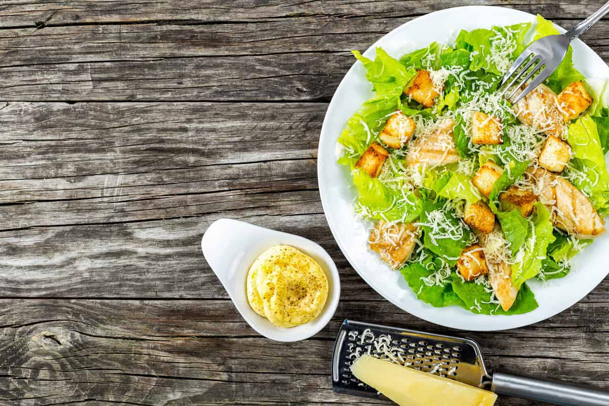 Delicious salad with croutons, grilled chicken breast, grated parmesan cheese and cos lettuce, with sauce in the gravy boat, simply and healthy recipe, horizontal top view